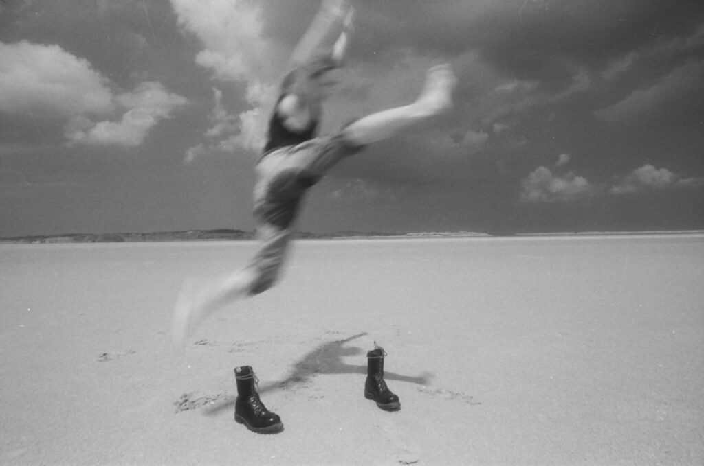 Junger, verschwommener Mann springt am Strand über ein Paar Springerstiefel
