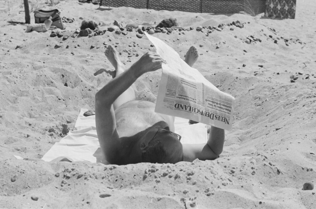 Nackter Mann liest am Strand eine Tageszeitung